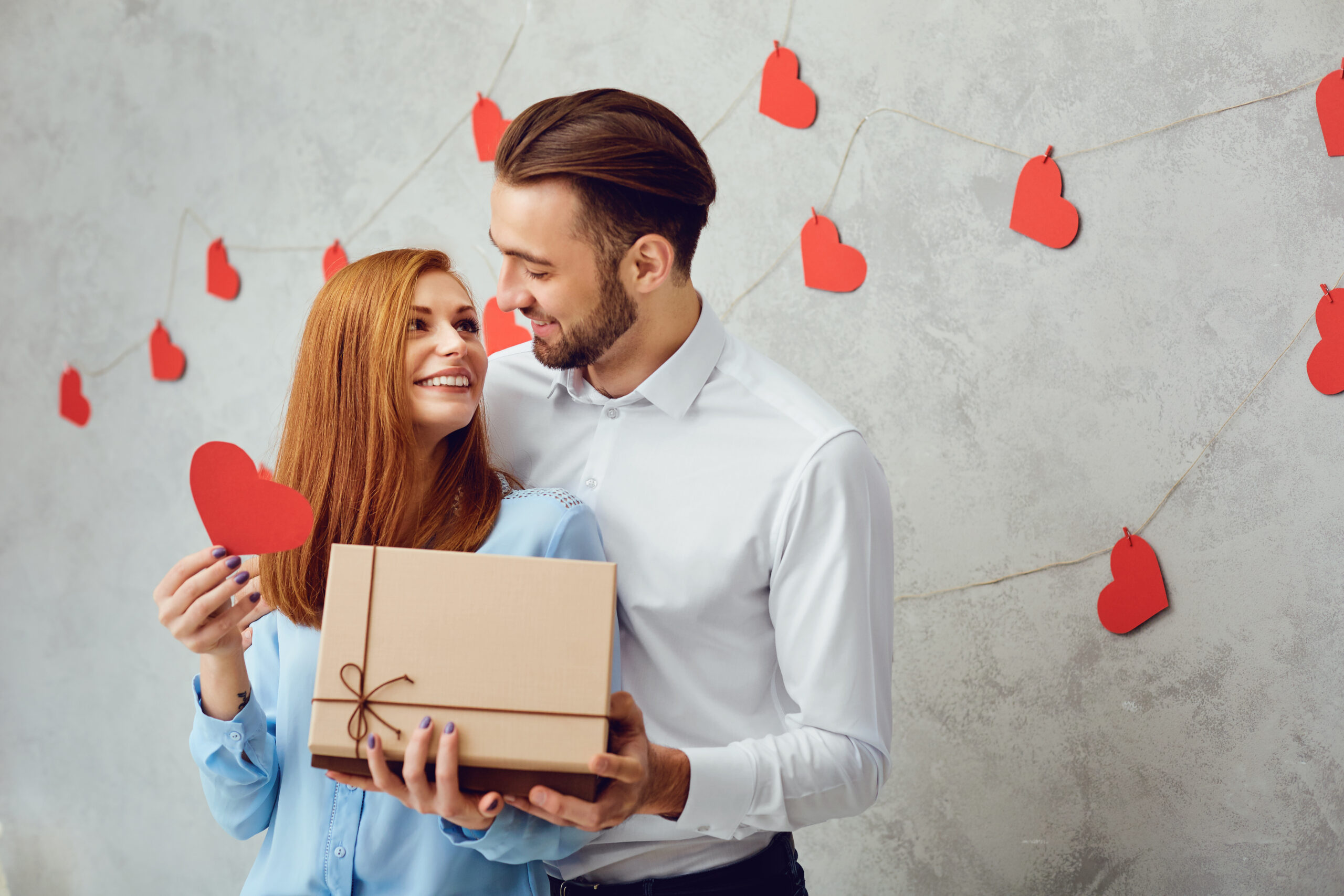 A young couple gives a gift on a gray background. Valentine's Day.